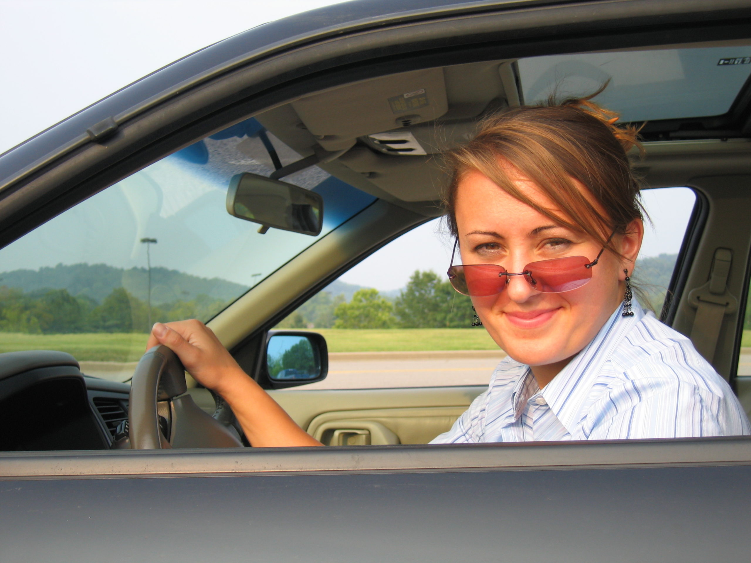 smiling woman driving car wearing sunglasses