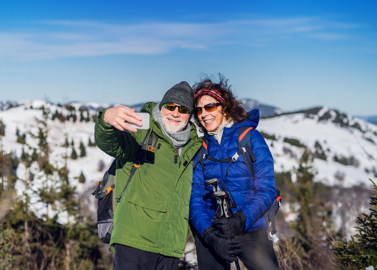 Senior couple hikers standing in snow-covered winter nature, taking selfie.